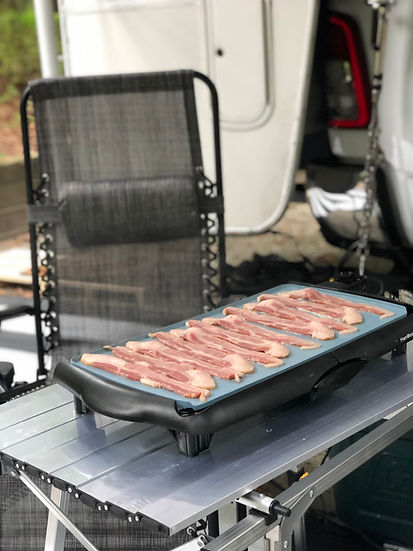 Bacon cooking on a griddle at a campsite.