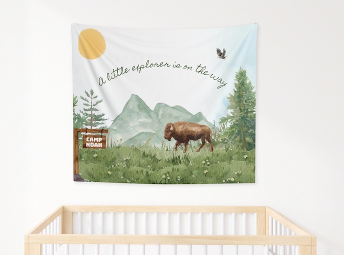 a wall tapestry featuring a watercolor mountain scene with trees, a buffalo and a wood trail sign