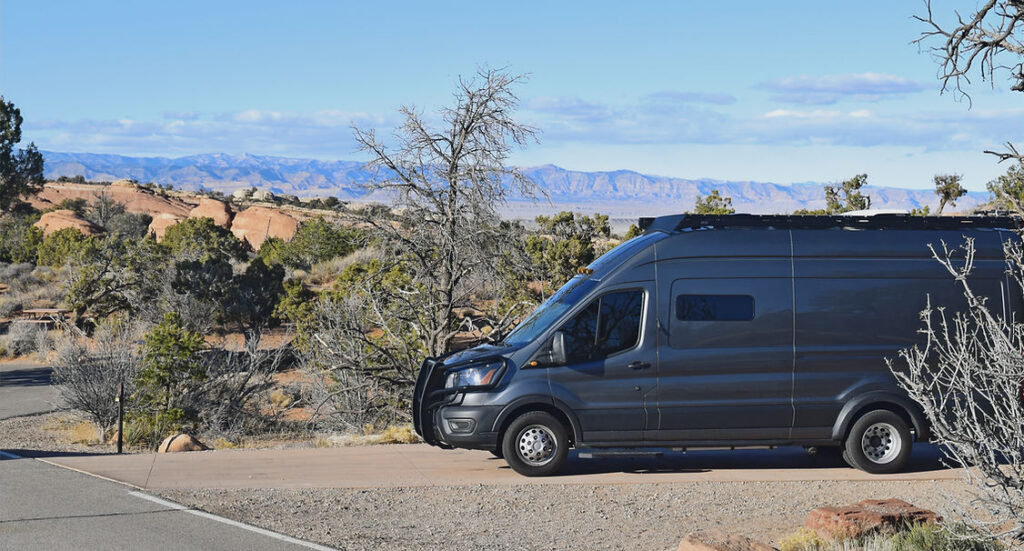 A gray van at a campsite in the desert.