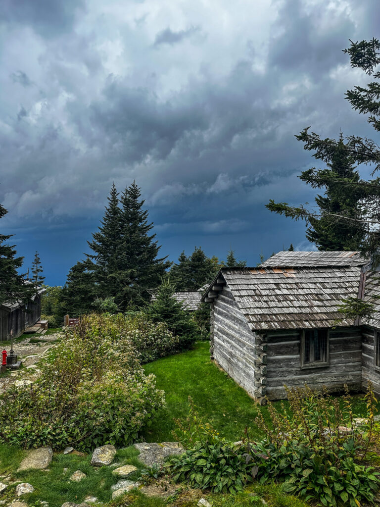 A view of dark clouds over the valley and wildflowers and a cabin from atop Mount Leconte.