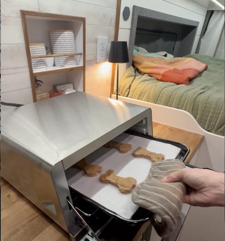 A van kitchen with a Ninja Foodie Flip on the counter top. A hand is pulling dog treats out of the oven.