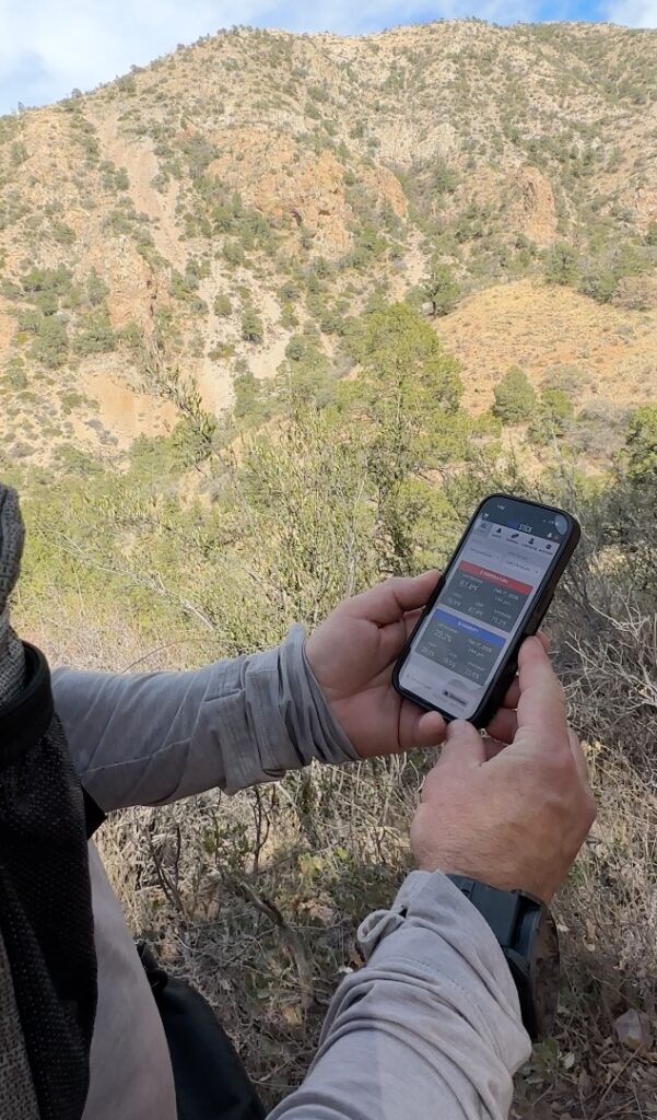 A man standing on a hiking trail in the desert viewing the temprature on the Temp Stick app on a cell phone.