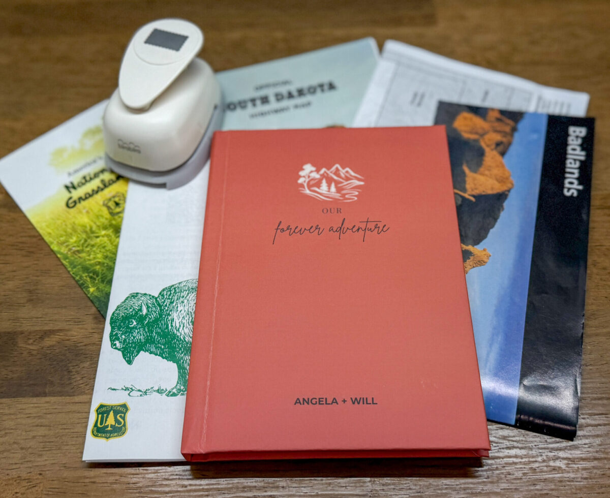 An orange or terracotta journal sitting on a table with some brochures, maps and a postage stamp punch.